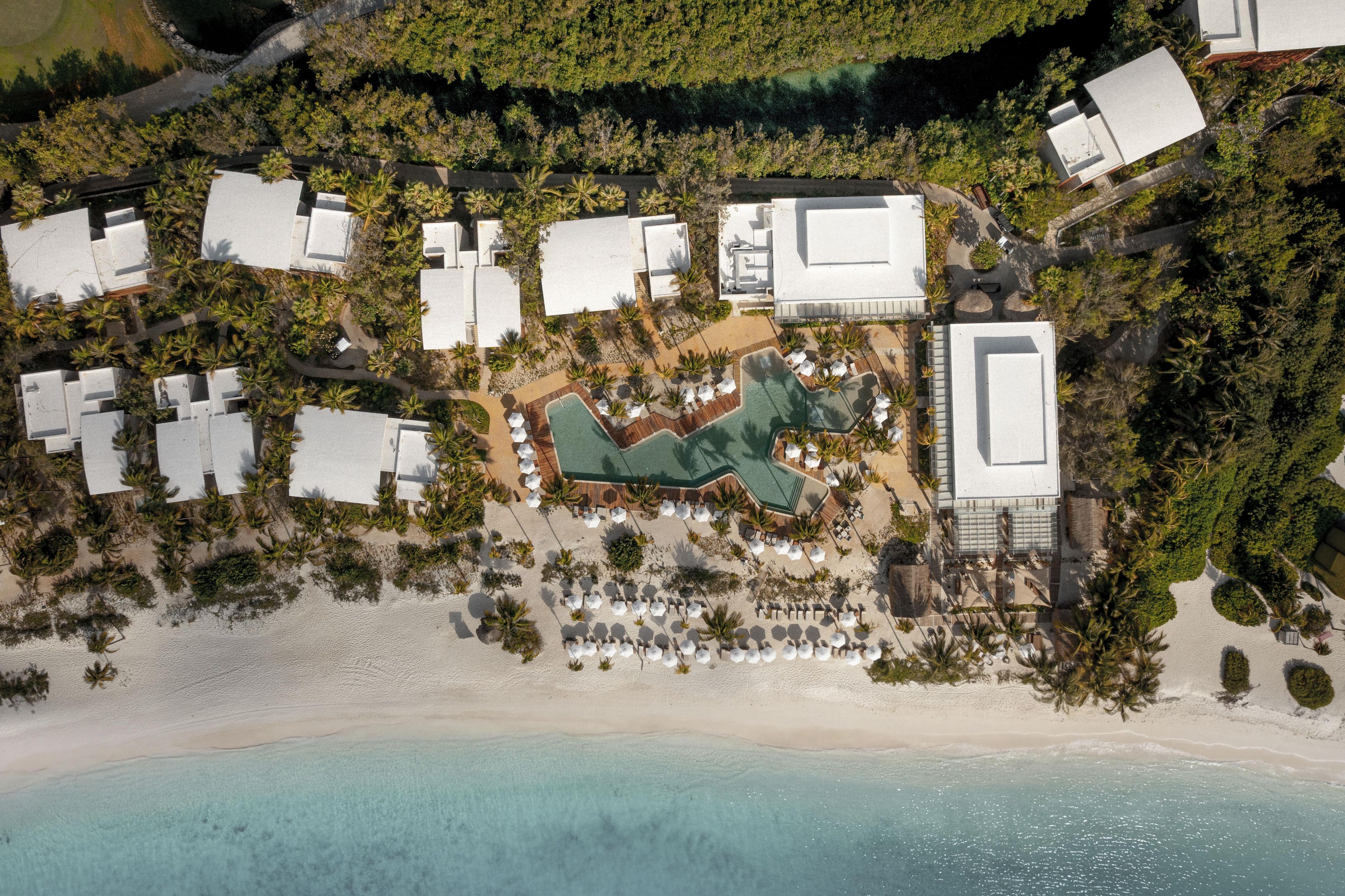 Vue aérienne d’un complexe hôtelier comprenant plusieurs bâtiments, un espace piscine et une plage.