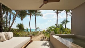 Een kamer met een bed, een klein tafeltje, een plafondventilator, uitzicht op het strand en een jacuzzi.