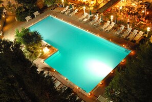 Una piscina rectangular con un borde de baldosas, rodeada de sillones de descanso y sombrillas.