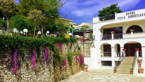 A two-story hotel with a stone wall and hanging flowers, a balcony, and a staircase leading to the upper floor. - Park Hotel Villa Americana (Rodi Garganico)