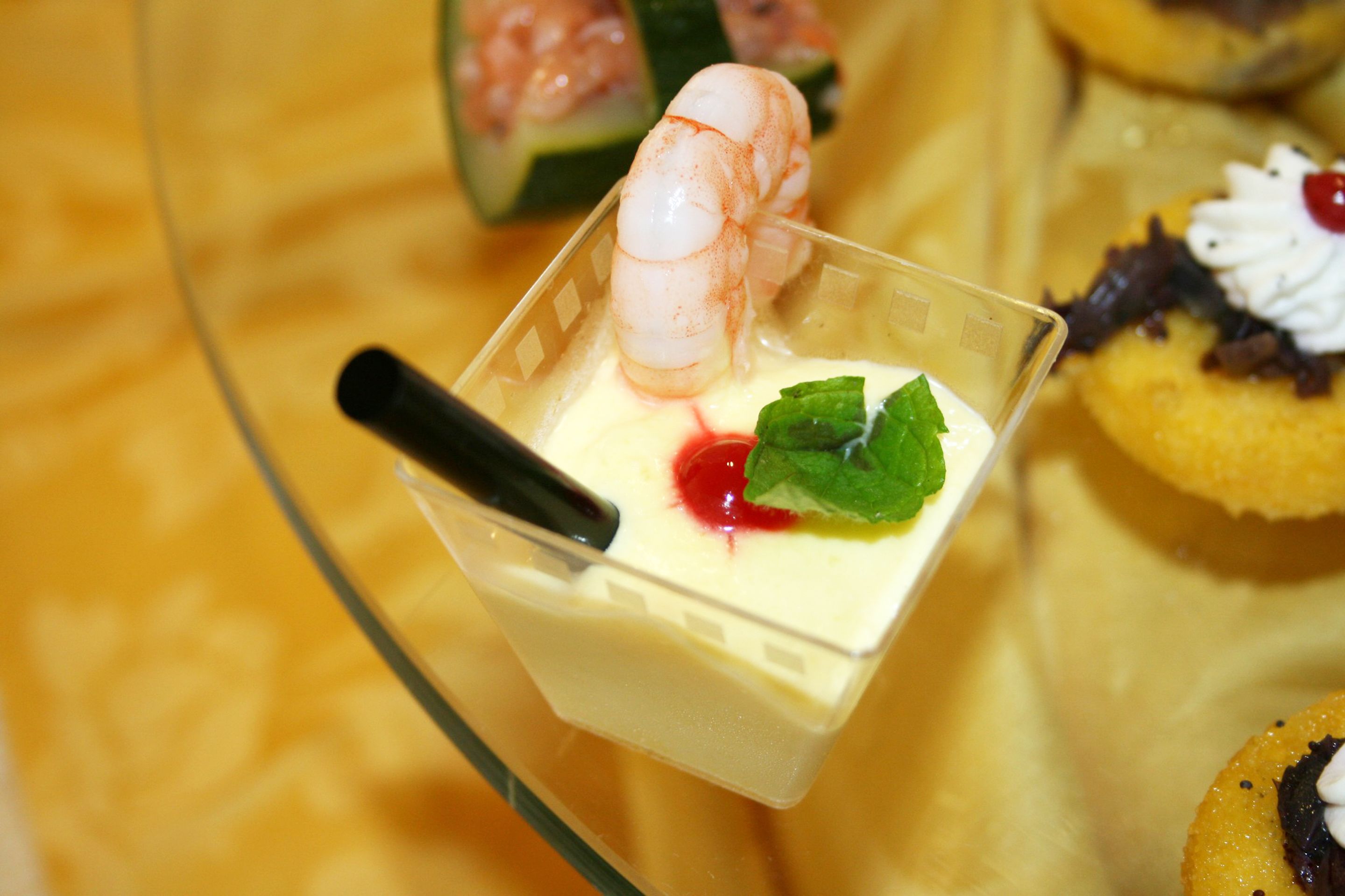Un dessert surmonté d’une crevette, décoré de menthe et nappé d’une sauce rouge, servi dans un verre transparent.