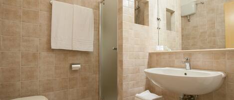 A bathroom with beige tiles, a toilet, a shower, a sink, and a mirror.