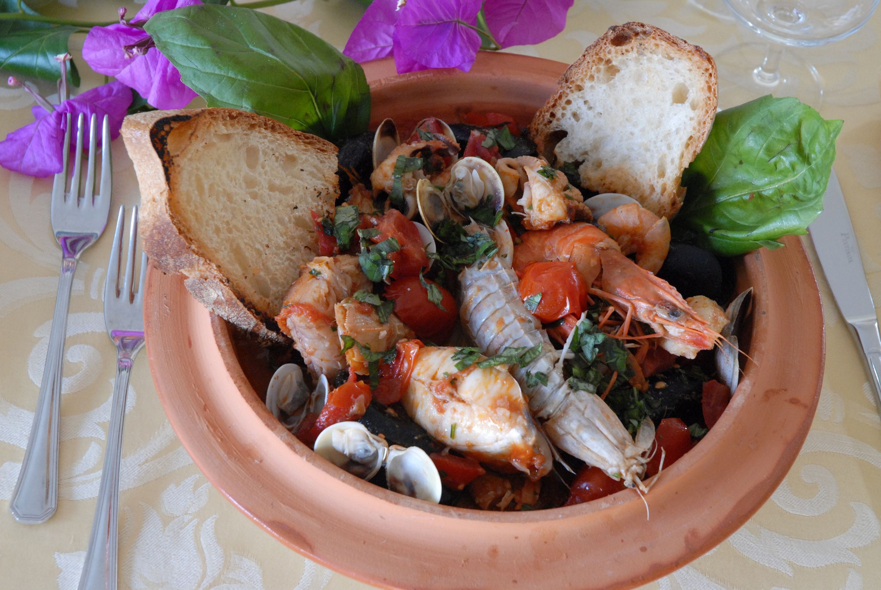A terracotta dish with seafood, bread, and basil on a tablecloth.