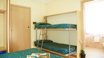 Ein Schlafsaalzimmer mit Etagenbetten, einem Schreibtisch, einem Stuhl, einer Topfpflanze und einem Badezimmer mit Waschbecken und Handtuchhalter.