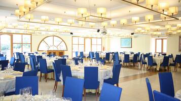Un amplio comedor con varias mesas dispuestas para un evento formal, con sillas azules y manteles blancos.