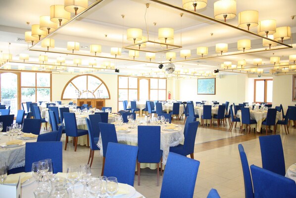 Un amplio comedor con varias mesas dispuestas para un evento formal, con sillas azules y manteles blancos.