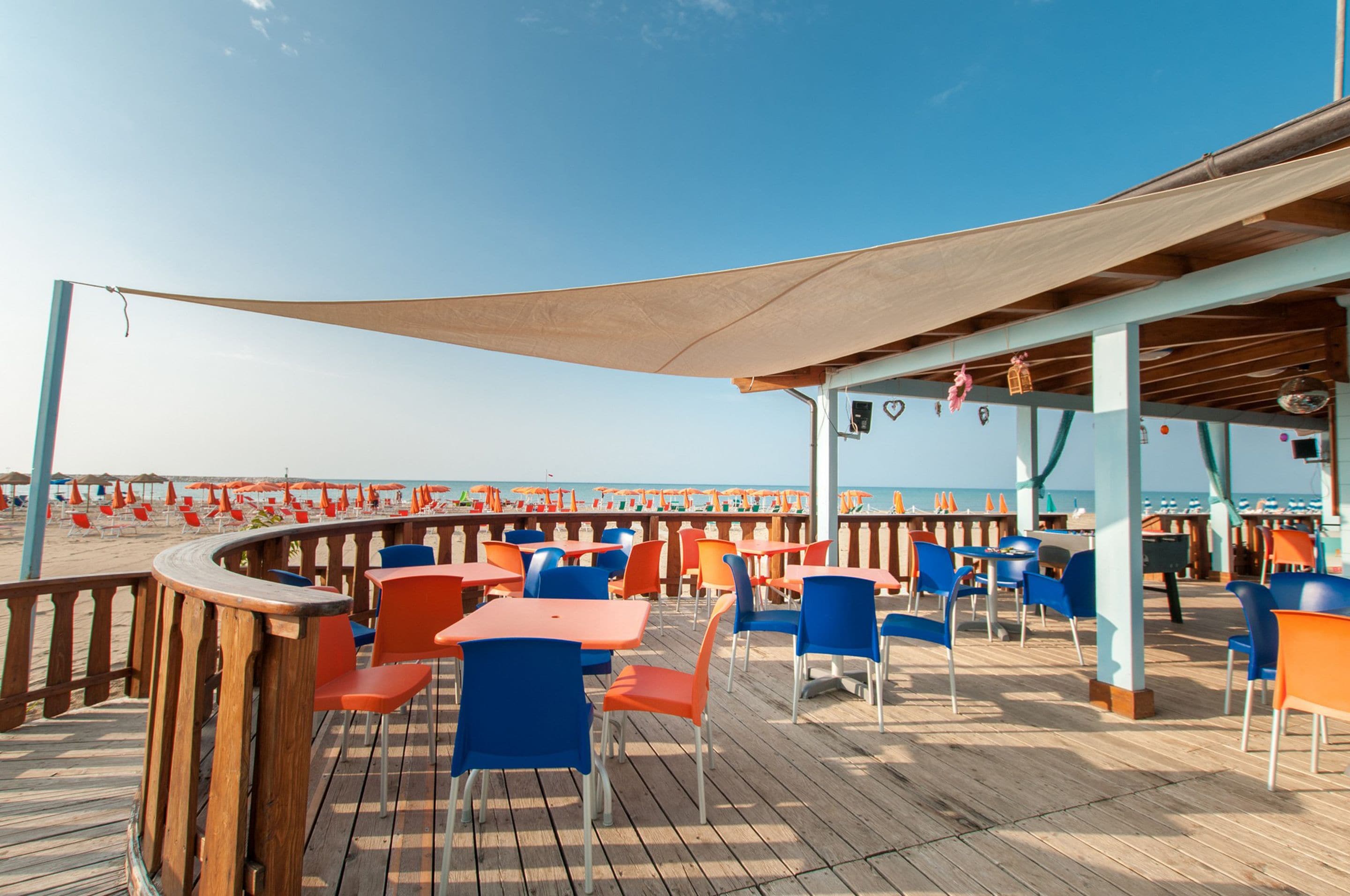 Een terras met tafels en stoelen, met uitzicht op een strand met parasols.