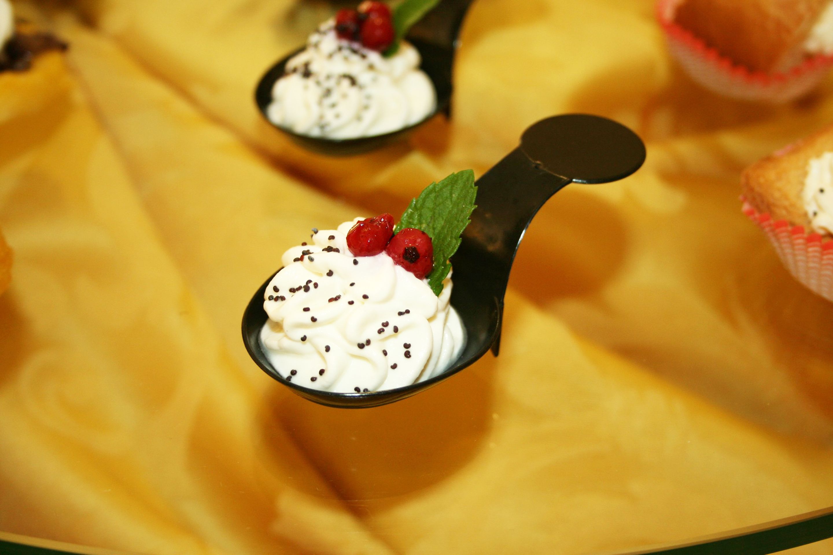A spoonful of dessert with whipped cream, berries, and chocolate shavings on a golden tablecloth.