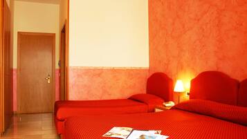 Ein Hotelzimmer mit zwei Betten, einer Holztür, einem Nachttisch mit Lampe und einem an der Wand befestigten Fernseher.