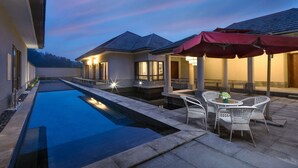 Piscina com área de terraço, mobiliário de jardim e céu ao pôr do sol.