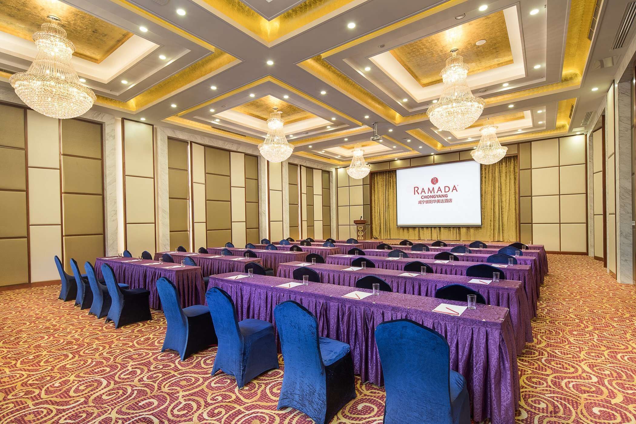 A conference room with rows of tables, blue chairs, and chandeliers.