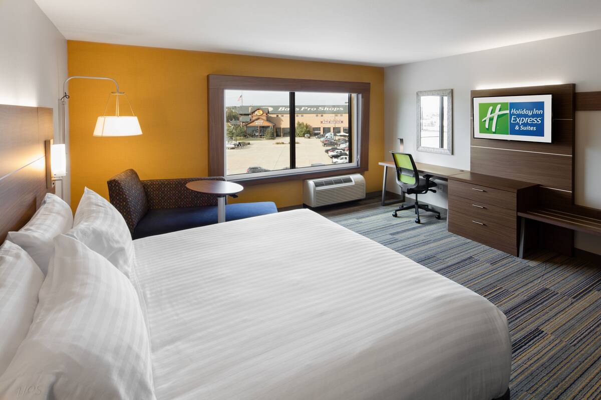 Une chambre d’hôtel avec un grand lit, un bureau, une chaise, une petite table, une lampe et un téléviseur affichant le logo de Holiday Inn Express.