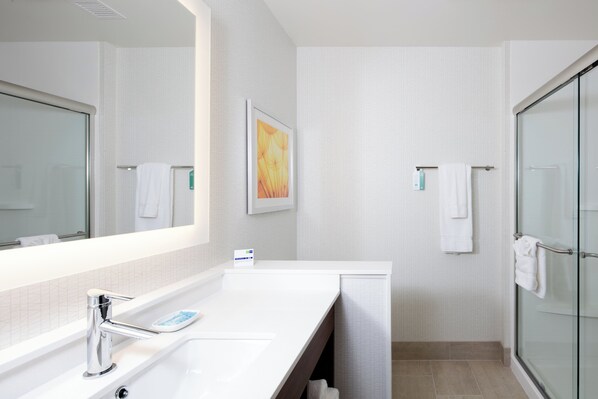 A modern bathroom with a large mirror, a white sink, a glass shower enclosure, and a framed artwork on the wall. - Holiday Inn Express & Suites East Peoria - Riverfront by IHG (East Peoria)