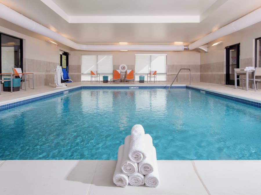 An indoor swimming pool with clear blue water, surrounded by lounge chairs and a stack of white towels.
