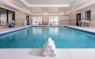 An indoor swimming pool with clear blue water, surrounded by lounge chairs and a stack of white towels.