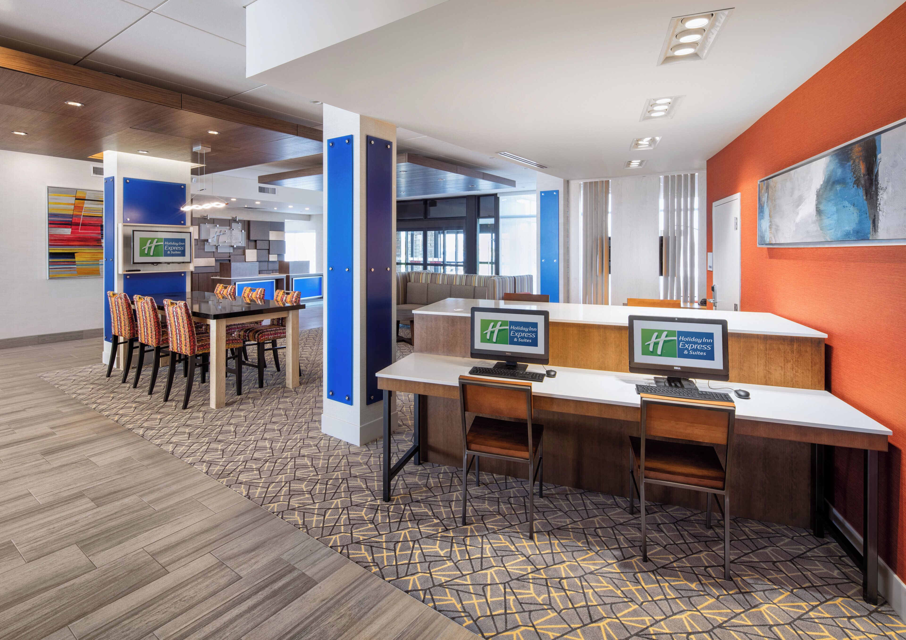 A hotel lobby with a reception desk, seating area, and a large abstract painting on the wall.
