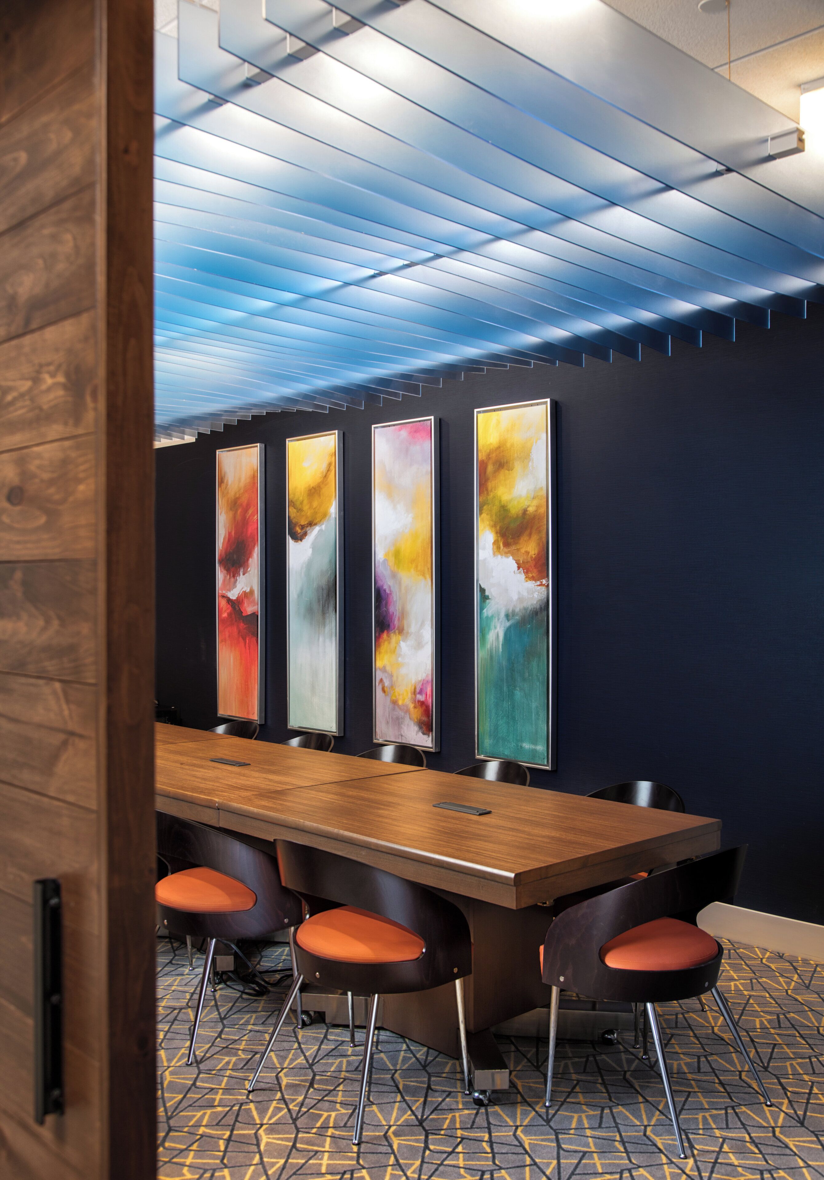 A conference room with a long table, four chairs, and abstract paintings on the wall.