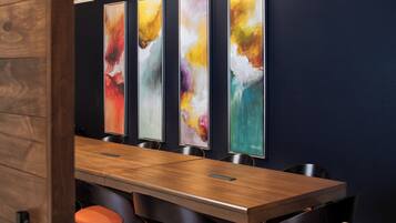 A conference room with a long table, four chairs, and abstract paintings on the wall.