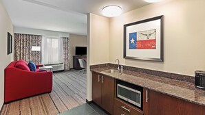 Habitación de hotel con sofá rojo, kitchenette con microondas, lavamanos y un cuadro de un toro en la pared.