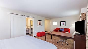 Habitación de hotel con cama, escritorio, sofá rojo, televisor y baño visible a través de una puerta abierta.