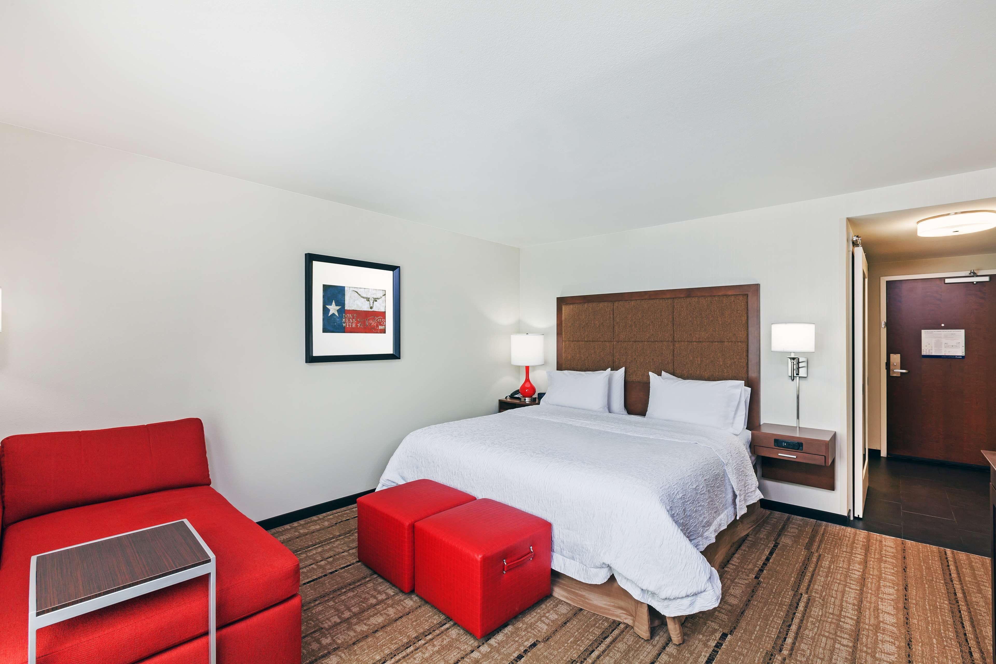 Una habitación de hotel con una cama grande, un sofá rojo, una mesita y un reposapiés rojo.