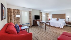 Una habitación de hotel con un sofá rojo, una cama con ropa blanca, un escritorio con computadora y un televisor.