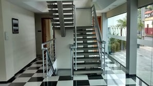A modern interior with a black and white checkered floor, a metal staircase, and a glass door leading outside. - Hotel Sollievo (Irati)