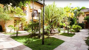 Un patio con un sendero adoquinado, un banco y diversas plantas tropicales.