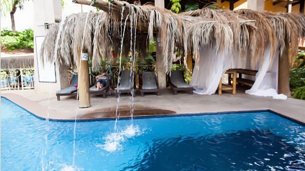 Un área de piscina con sillones de descanso y una estructura de techo de paja.