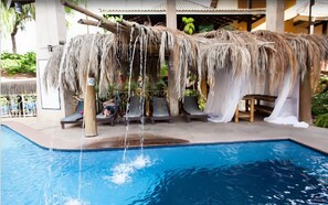 Uma área de piscina com espreguiçadeiras e uma estrutura de palha.