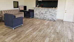A living room with a sofa, armchair, and a kitchen area with a stone backsplash. - Inn of Rockwall (Rockwall)