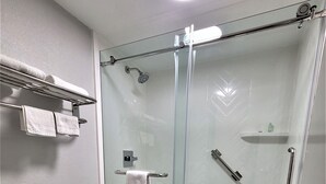 A bathroom with a glass-enclosed shower, a toilet, and a towel rack with towels. - Inn of Rockwall (Rockwall)