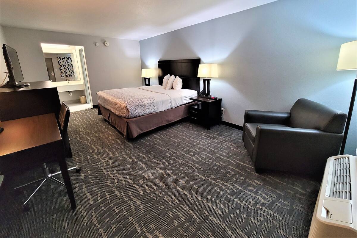 A hotel room with a bed, a desk, a chair, and a lamp.