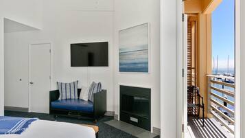 A hotel room with a bed, a sofa, a flat-screen TV, a fireplace, and a balcony with a view of the marina.