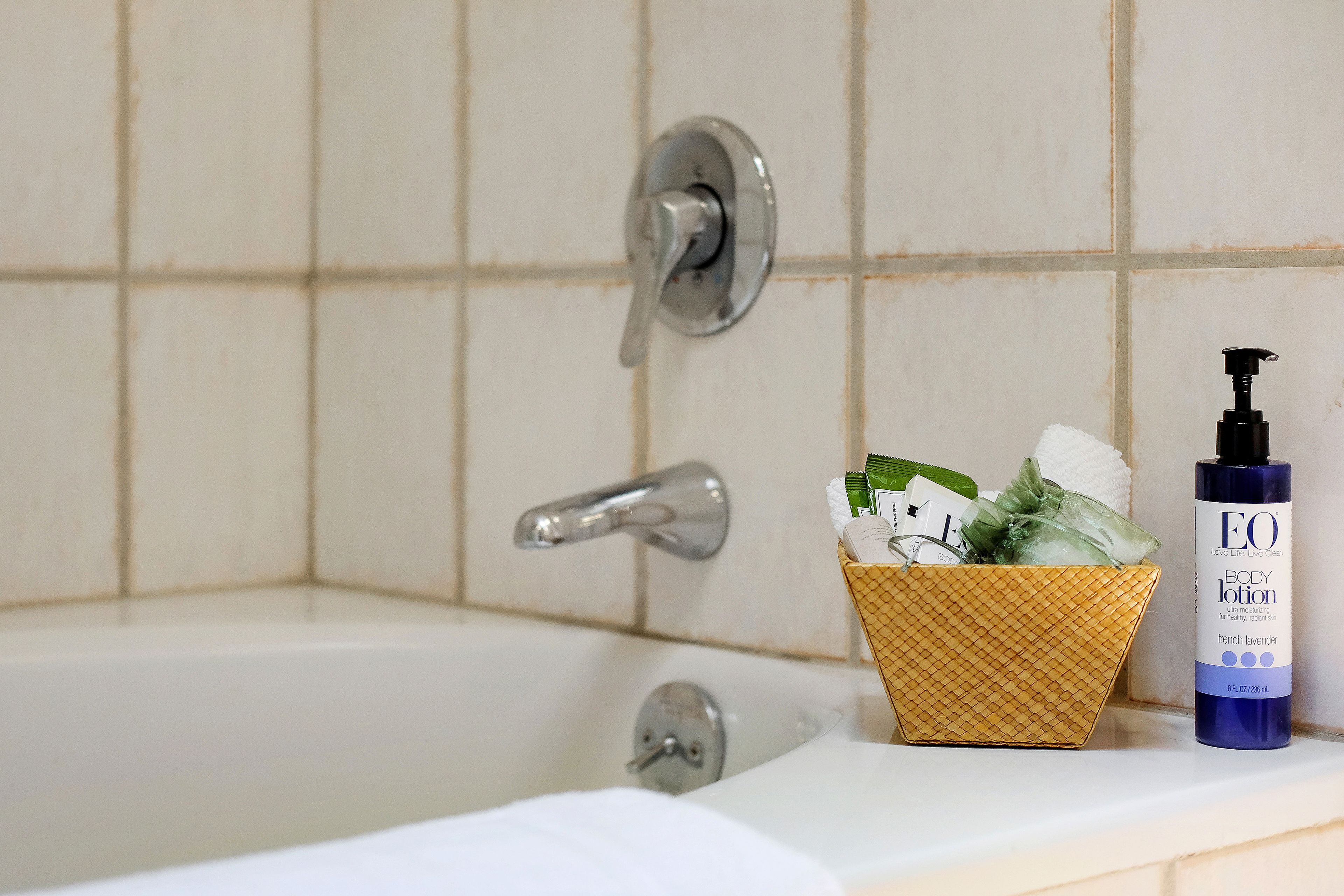 A bathroom with a bathtub, a towel, and toiletries including a bottle of body lotion.