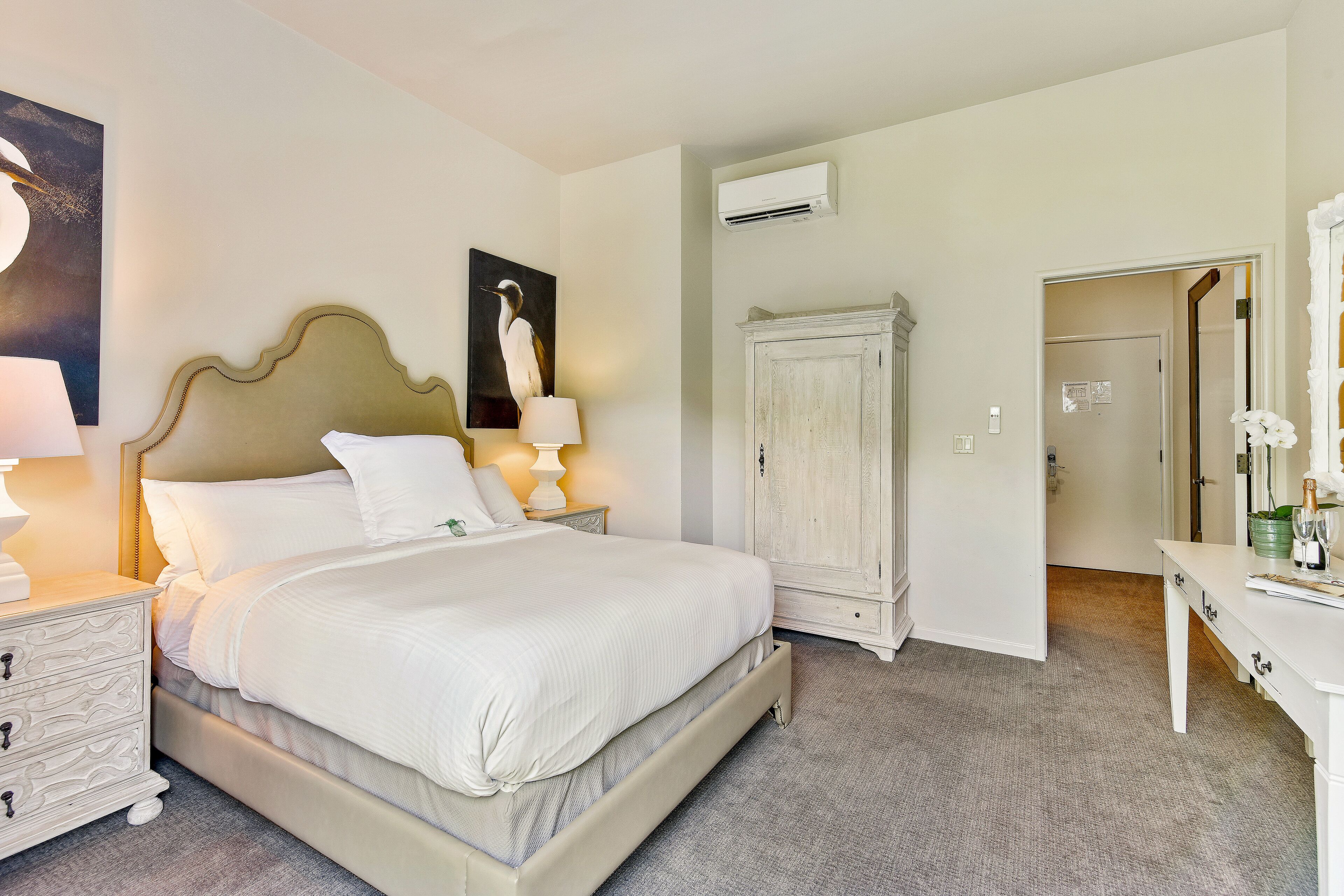A neatly arranged bedroom with a bed, bedside tables, a wardrobe, and a desk with a lamp.