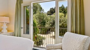 A hotel room with a bed, a chair, a lamp, and a balcony with a view of trees and a garden. - Mill Valley Inn (Mill Valley)
