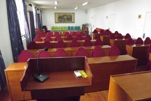 Une salle de conférence avec des rangées de chaises rouges, un pupitre et un microphone.