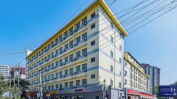 Ett hotell med flera våningar, en gul fasad, flera balkonger och ett antal butiker på markplan.