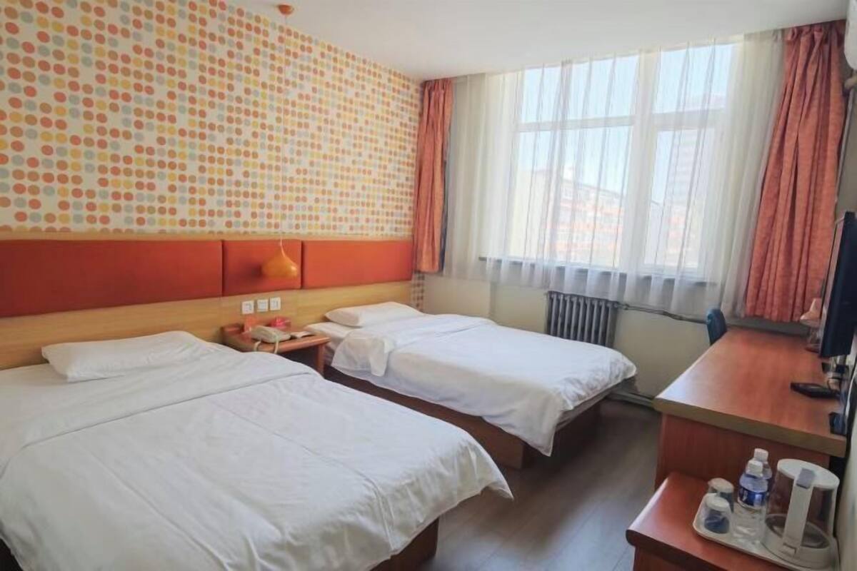 A hotel room with two beds, a desk, a telephone, and a window with curtains.