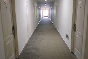 Un pasillo largo y estrecho con puertas a ambos lados, que conduce a una salida luminosa al final.