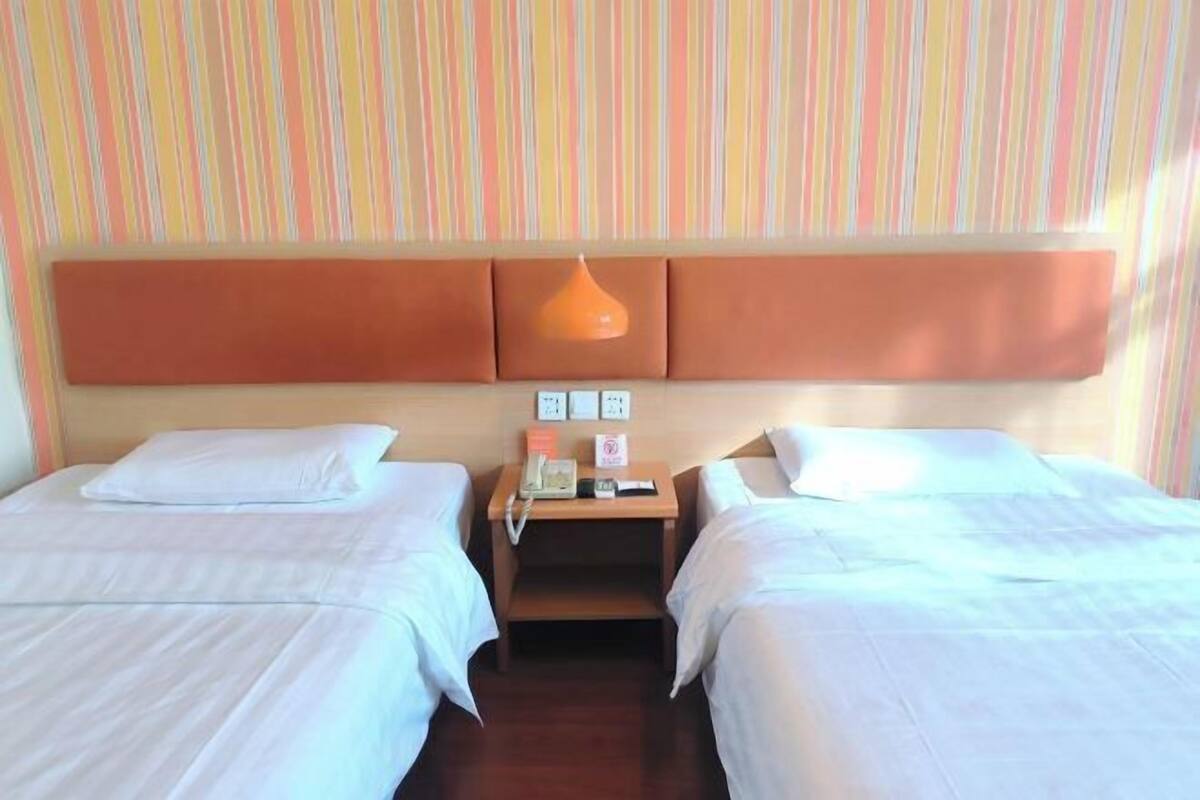A hotel room with two beds, a wooden nightstand, a telephone, and a wall-mounted light fixture.