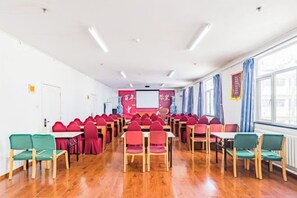 Een vergaderzaal met rijen tafels en stoelen, een scherm voor een beamer en een groot raam.