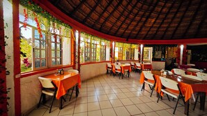 Un restaurante con techo de paja, suelo de baldosas y mesas con manteles anaranjados.