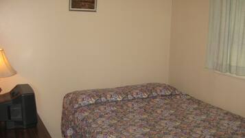 Un dormitorio con colcha estampada, lámpara de noche, un cuadro en la pared y una ventana con cortinas.
