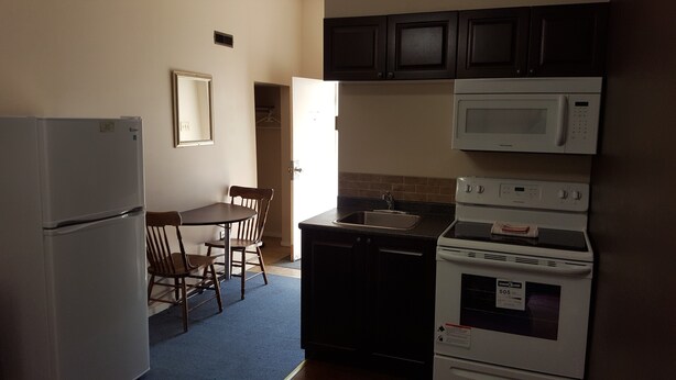 A compact kitchen with a refrigerator, microwave, stove, and sink. There is a dining table with chairs. - Hat Motel (Medicine Hat)
