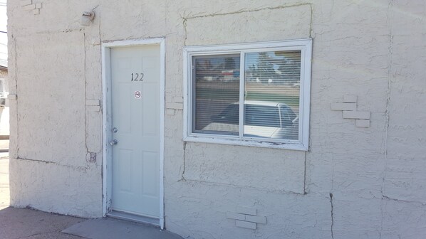 A white door with the number 122, a small window with blinds, and a textured wall.