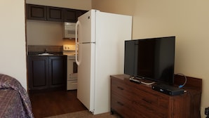 A compact kitchen with a refrigerator, microwave, and stove. A flat-screen TV is mounted on a wooden dresser. - Hat Motel (Medicine Hat)