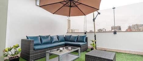 A rooftop patio with a sectional sofa, a coffee table, and an umbrella.