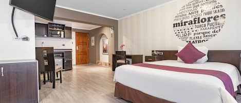 A modern hotel room with a large bed, a desk, and a kitchenette.